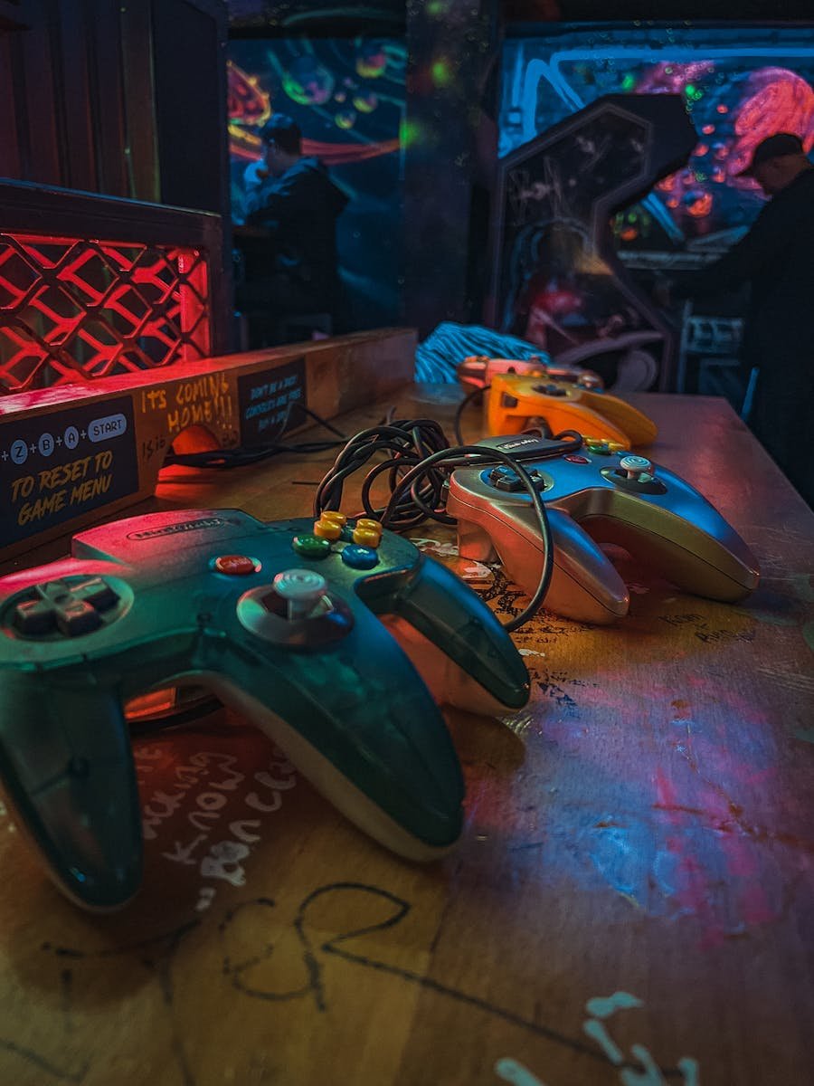Close-up of vintage gaming controllers on a colorful wooden desk in an arcade setting.
