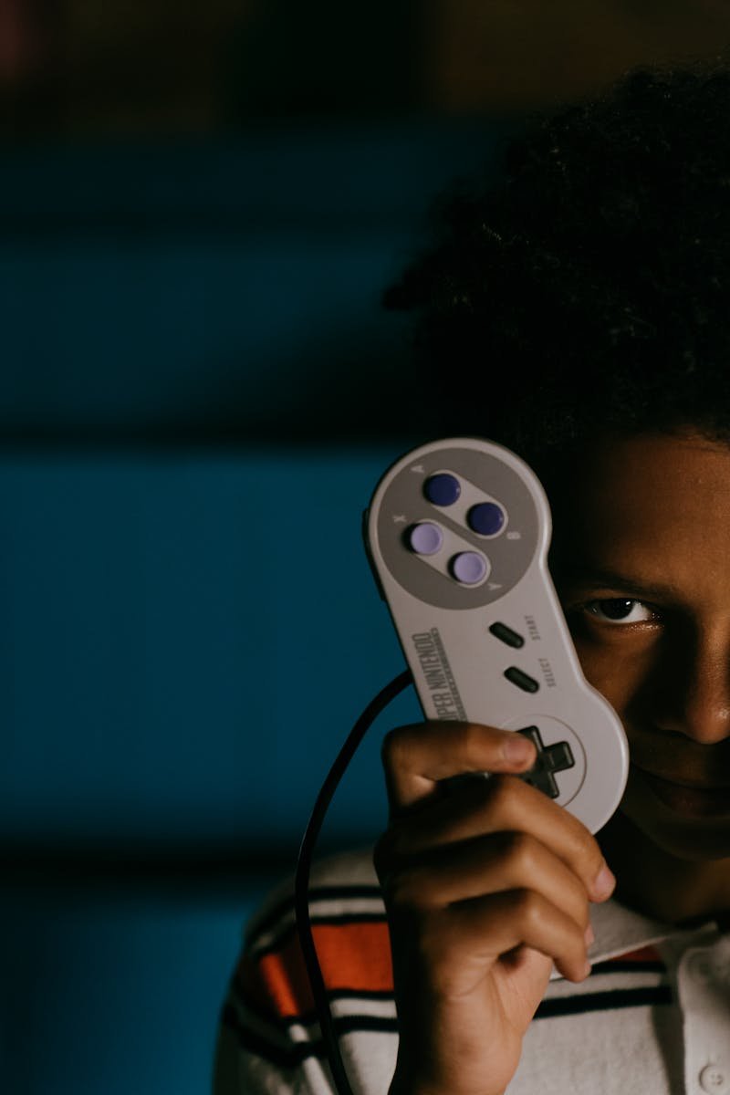 Close-up of a young man holding a vintage gaming controller, indoors at night.