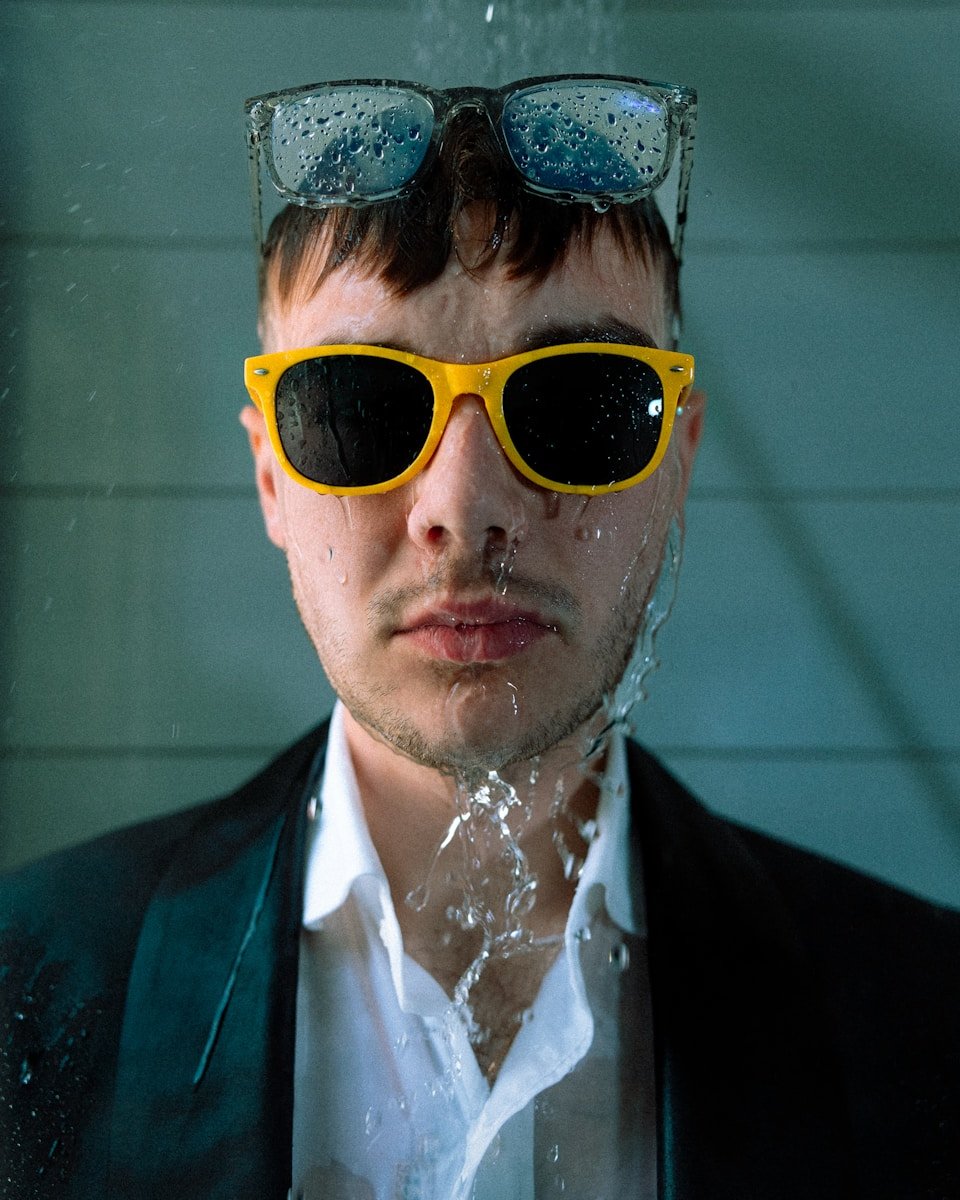 Man wearing sunglasses with water falling on him